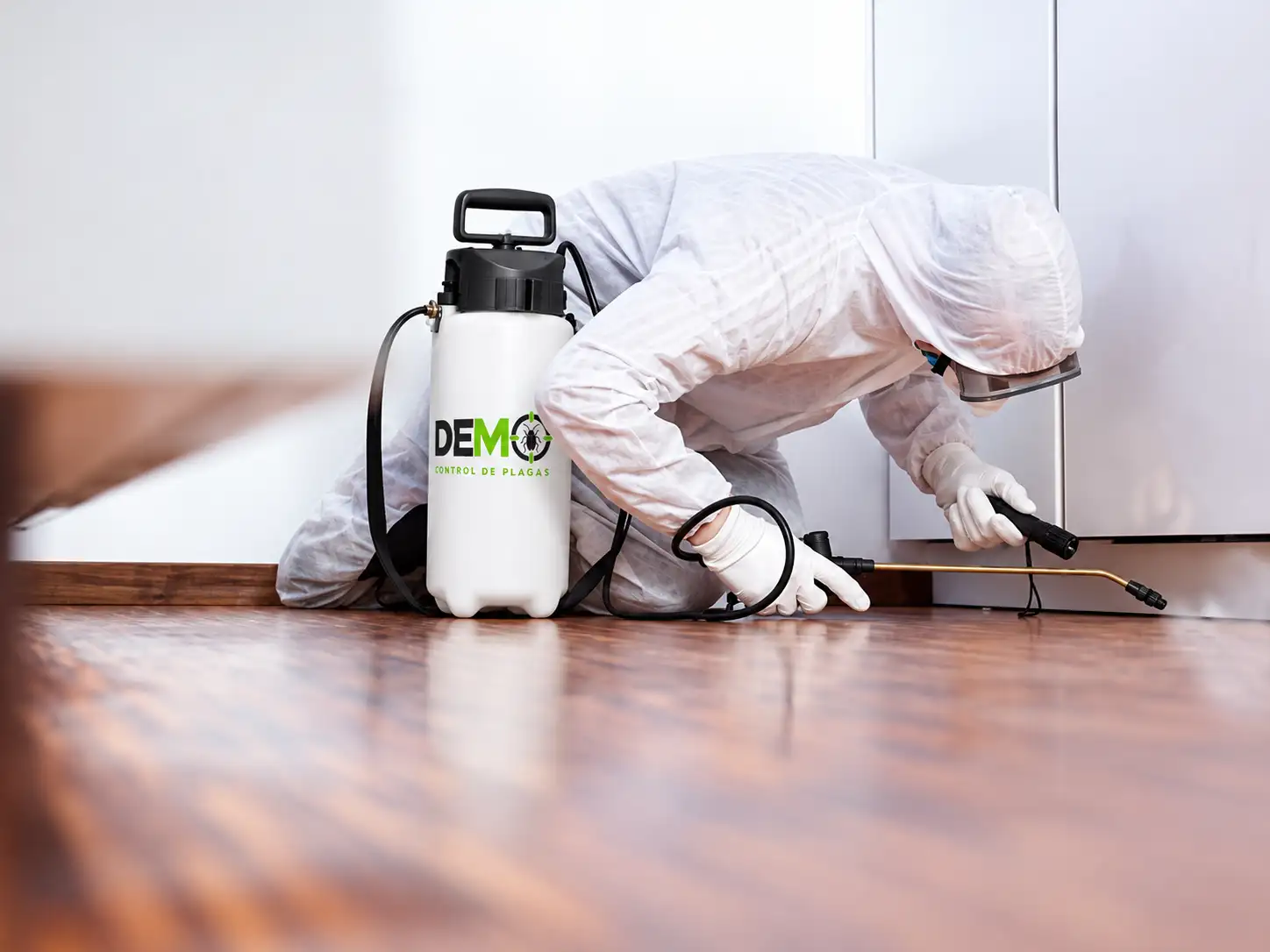 Técnico con traje de protección blanco aplicando en la base de los gabinetes de una cocina